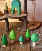 Bajo green forest tree set wooden toy figures placed on a wooden desk in the Babipur playroom with a Magic Wood adventure playground in the background.