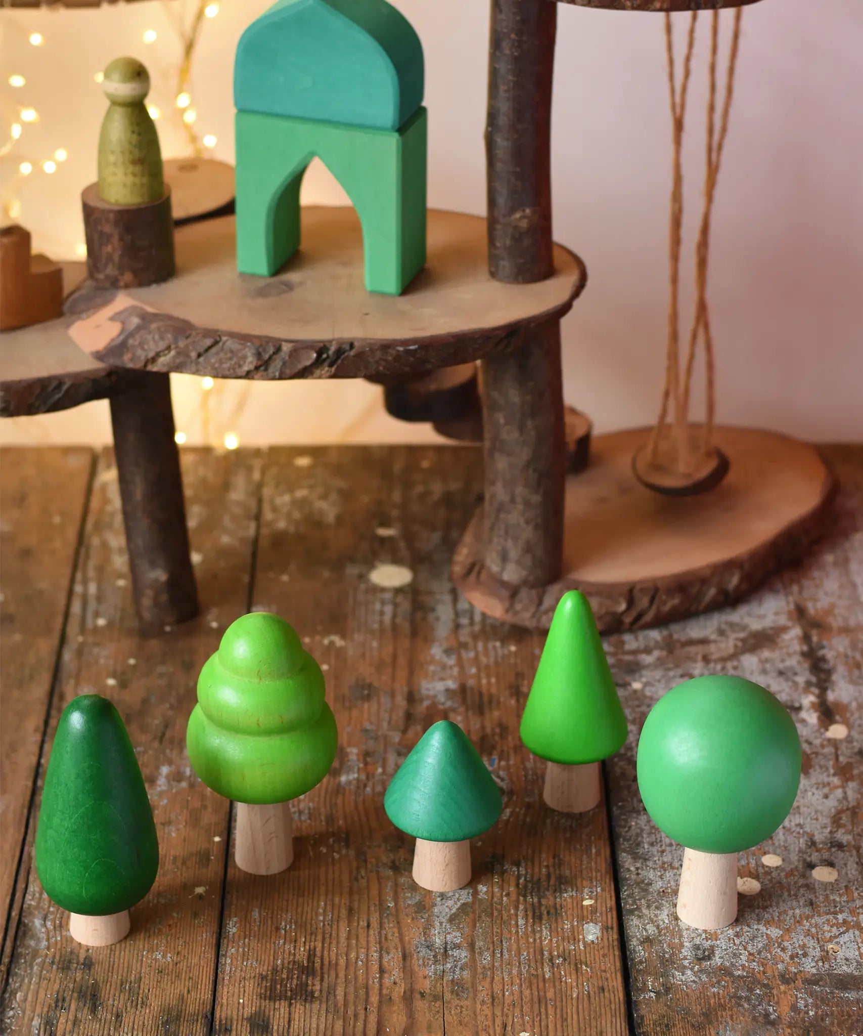 Bajo green forest tree set wooden toy figures placed on a wooden desk in the Babipur playroom with a Magic Wood adventure playground in the background.