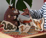 Bajo Gruffalo character puzzle pieces placed on a rattan stool next to a Bajo Gruffalo wooden figure.