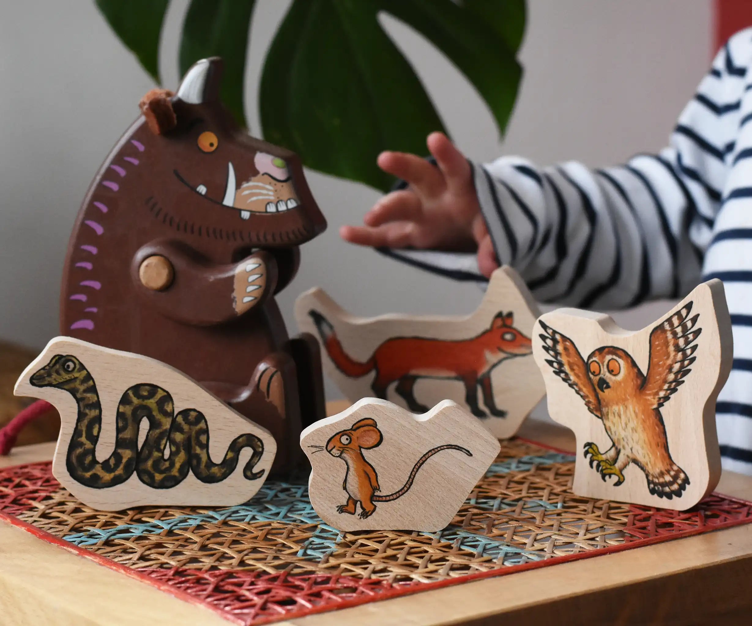Bajo Gruffalo character puzzle pieces placed on a rattan stool next to a Bajo Gruffalo wooden figure.