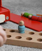 A close up of one of the blue peg dolls from the Bajo London bus wooden toy placed on the wooden floor base from the bus.  These heirloom quality toys by Bajo are part of a wide range of wooden toys available here at Babipur