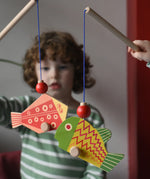 Bajo magnetic fishing game toy. Children holding wooden rodd with red and yellow fish attached.