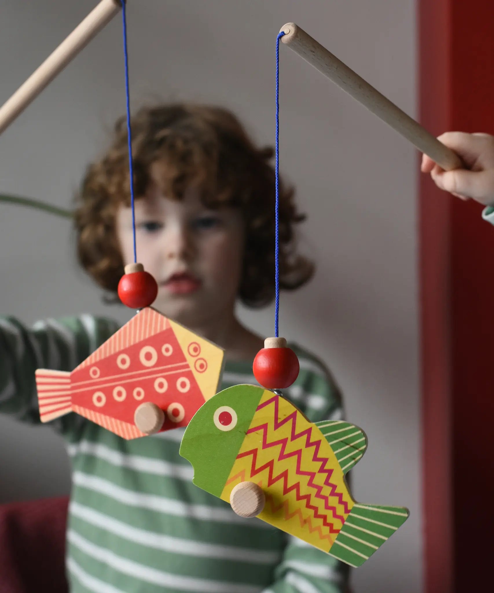 Bajo magnetic fishing game toy. Children holding wooden rodd with red and yellow fish attached.