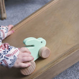 A close up of a child's hand pushing a mint green coloured small rabbit push along toy up a Trivlimb Miri slide.  These heirloom quality toys by Bajo are part of a wide range of wooden toys available here at Babipur.