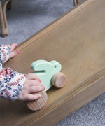A close up of a child's hand pushing a mint green coloured small rabbit push along toy up a Trivlimb Miri slide.  These heirloom quality toys by Bajo are part of a wide range of wooden toys available here at Babipur.