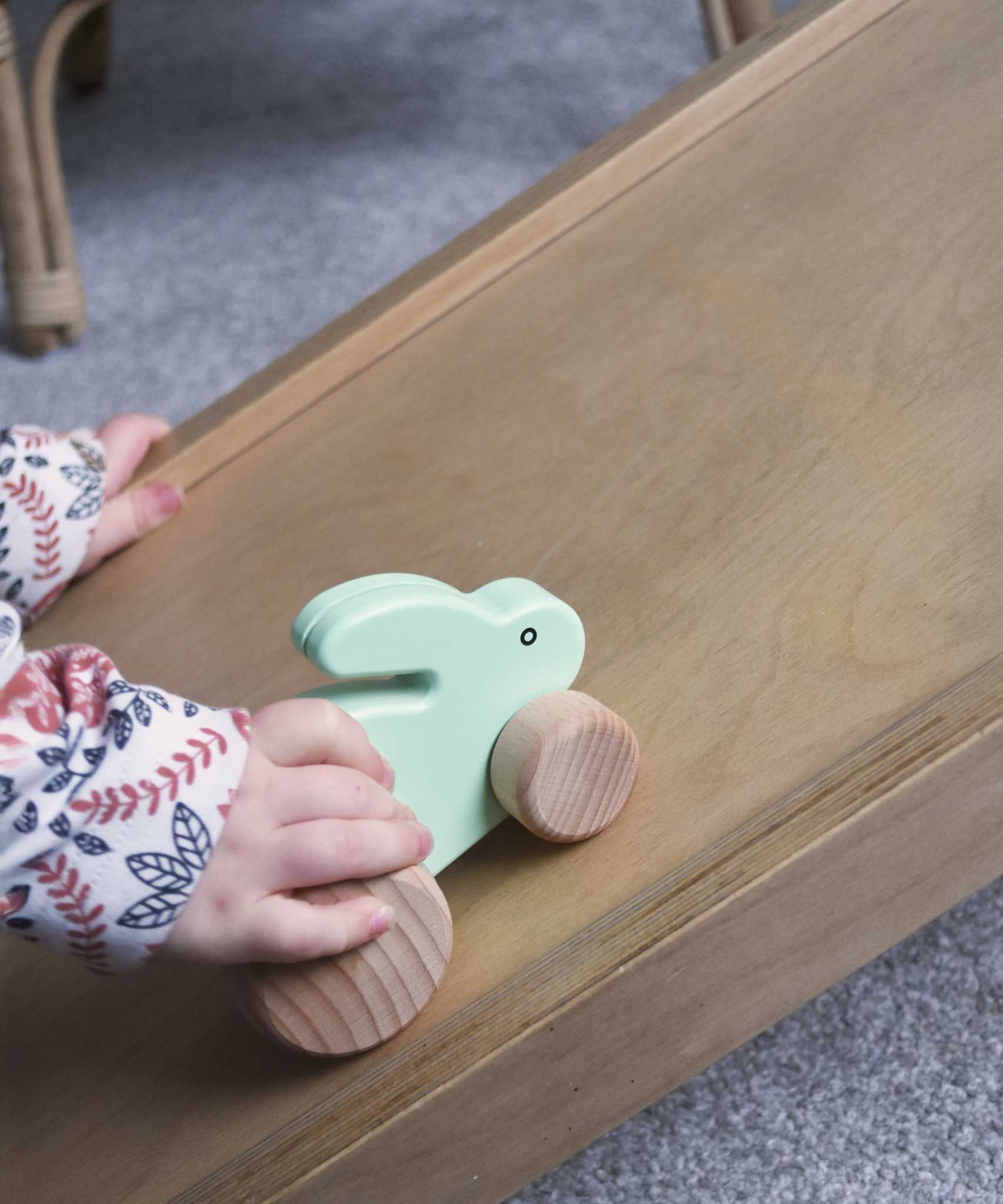 A close up of a child's hand pushing a mint green coloured small rabbit push along toy up a Trivlimb Miri slide.  These heirloom quality toys by Bajo are part of a wide range of wooden toys available here at Babipur.