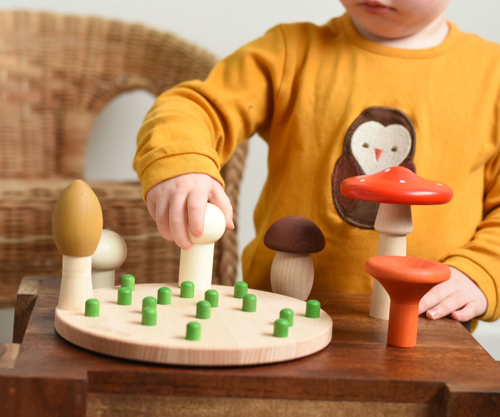 A child playing with the Bajo Wooden Mushroom Forest Peg Puzzle. The child is placing the white button mushroom on one of the green pegs on the wooden base.  These heirloom quality toys by Bajo are part of a wide range of wooden toys available here at Babipur. 