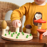 A child playing with the Bajo Wooden Mushroom Forest Peg Puzzle. The child is placing the white button mushroom on one of the green pegs on the wooden base.  These heirloom quality toys by Bajo are part of a wide range of wooden toys available here at Babipur. 