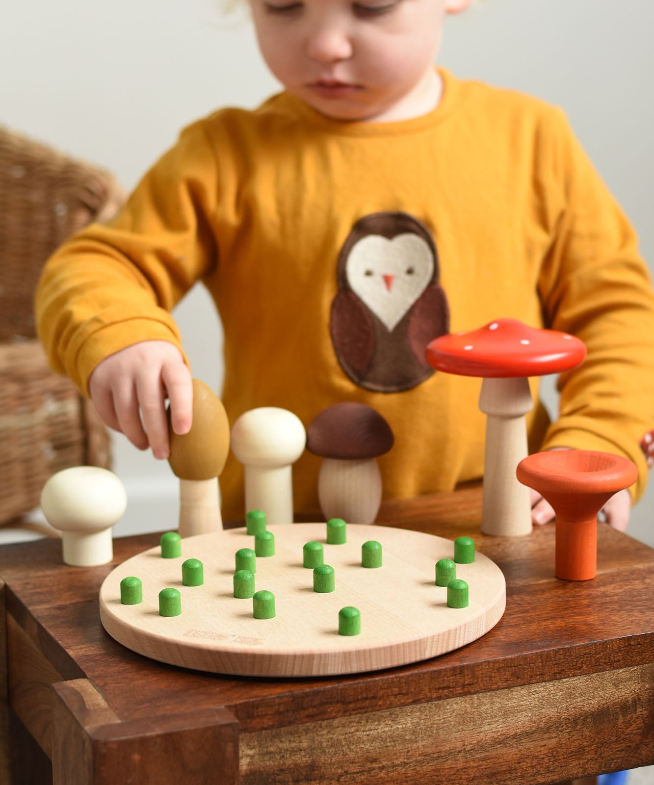 A child playing with the Bajo Wooden Mushroom Forest Peg Puzzle. The child is picking up the yellow coloured mushroom. These heirloom quality toys by Bajo are part of a wide range of wooden toys available here at Babipur. 