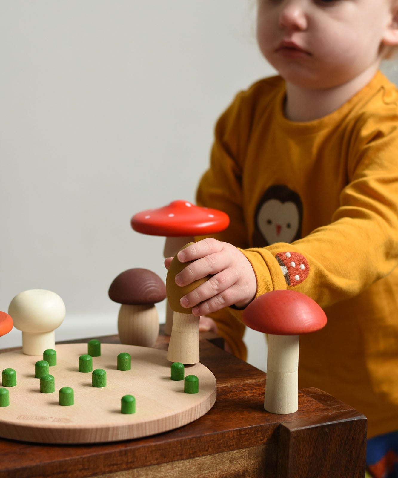 A child playing with the Bajo Wooden Mushroom Forest Peg Puzzle. The child is picking up the yellow coloured mushroom from the base. These heirloom quality toys by Bajo are part of a wide range of wooden toys available here at Babipur. 