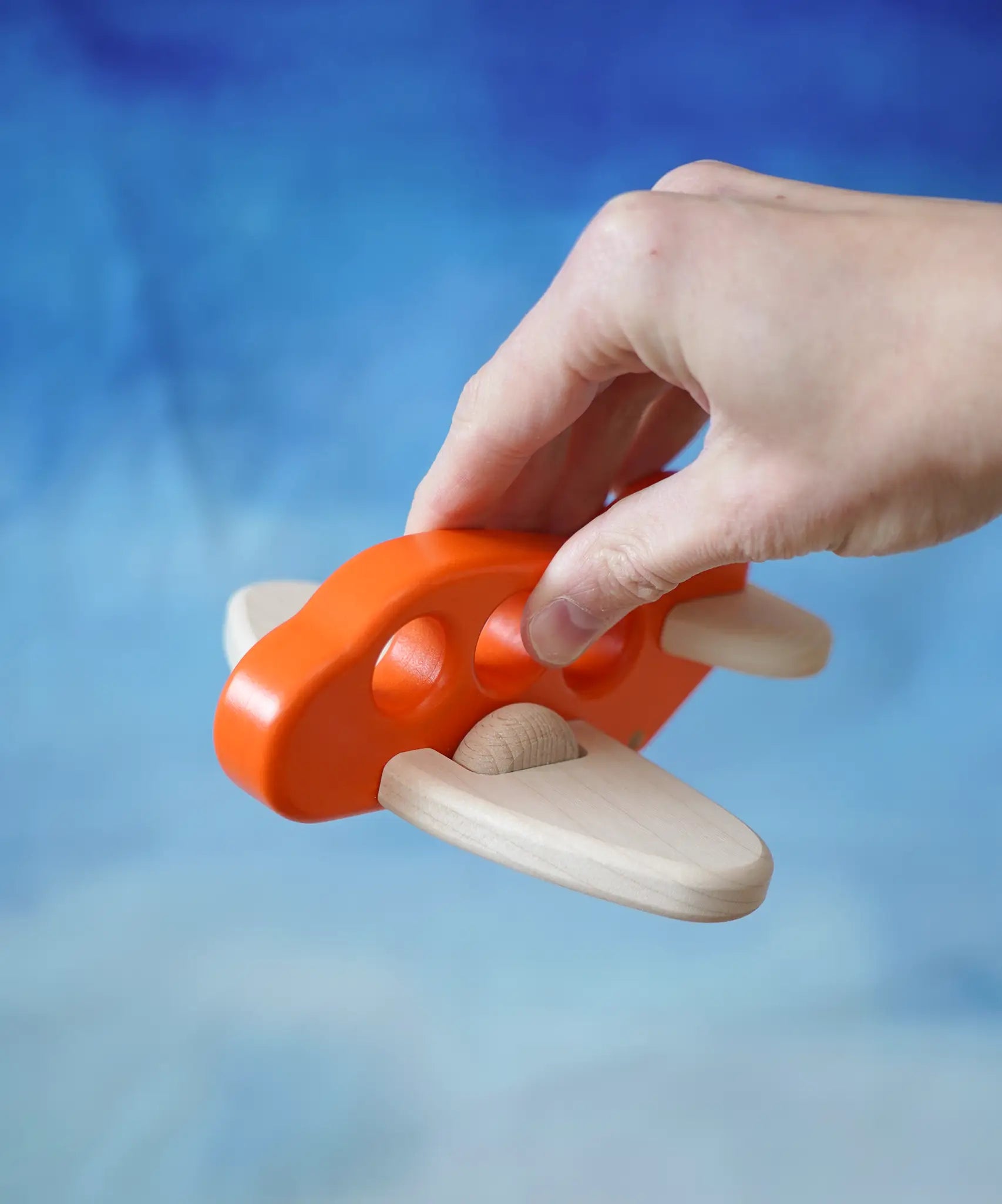 Adult hand holding a Bajo Toys wooden push along airplane in orange showing scale
