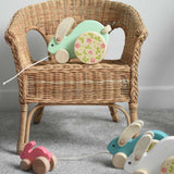 A mint green coloured big Bajo rabbit placed on a child's wicker chair. Other Bajo rabbits can be seen placed on the floor in front of the chair.  These heirloom quality toys by Bajo are part of a wide range of wooden toys available here at Babipur.