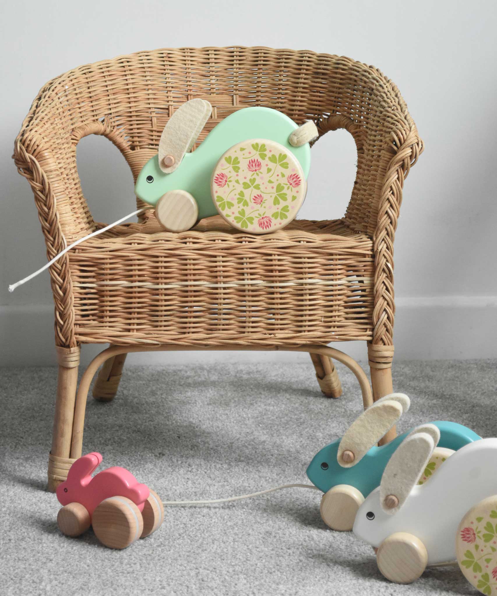 A mint green coloured big Bajo rabbit placed on a child's wicker chair. Other Bajo rabbits can be seen placed on the floor in front of the chair.  These heirloom quality toys by Bajo are part of a wide range of wooden toys available here at Babipur.