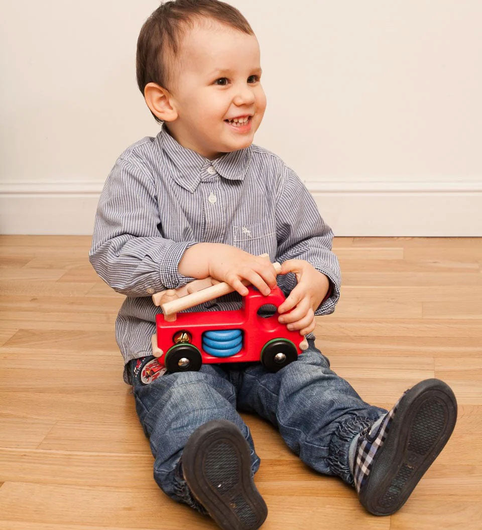 A child sitting on the floor playing with the Bajo Fire Engine wooden toy vehicle. 