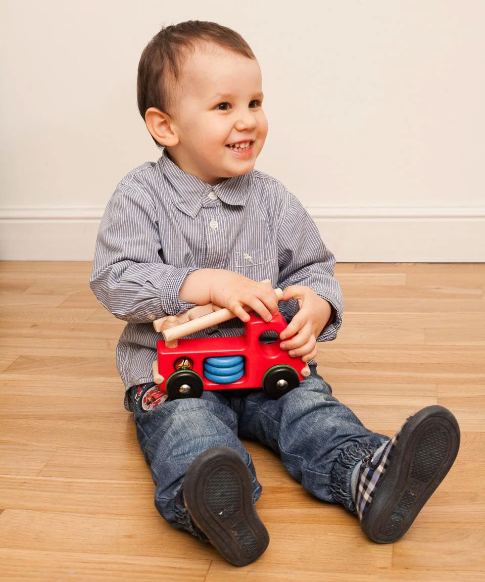 A child sitting on the floor playing with the Bajo Fire Engine wooden toy vehicle. 