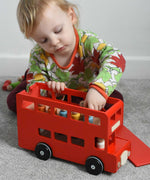 A child playing with the Bajo London bus wooden toy. The child has taken the roof off and is taking the wooden peg dolls off the floor of the bus. These heirloom quality toys by Bajo are part of a wide range of wooden toys available here at Babipur. 