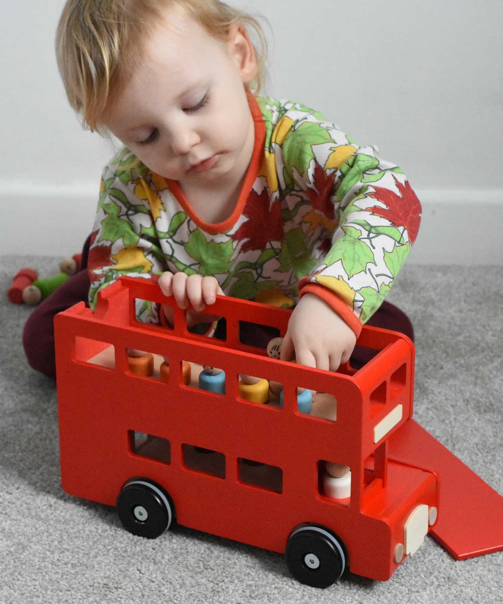 A child playing with the Bajo London bus wooden toy. The child has taken the roof off and is taking the wooden peg dolls off the floor of the bus. These heirloom quality toys by Bajo are part of a wide range of wooden toys available here at Babipur. 