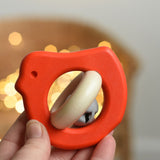 A red coloured Bajo Wooden Bird Baby Rattle with Bell shown in an adult's hand. These heirloom quality toys by Bajo are part of a wide range of wooden toys available here at Babipur. 
