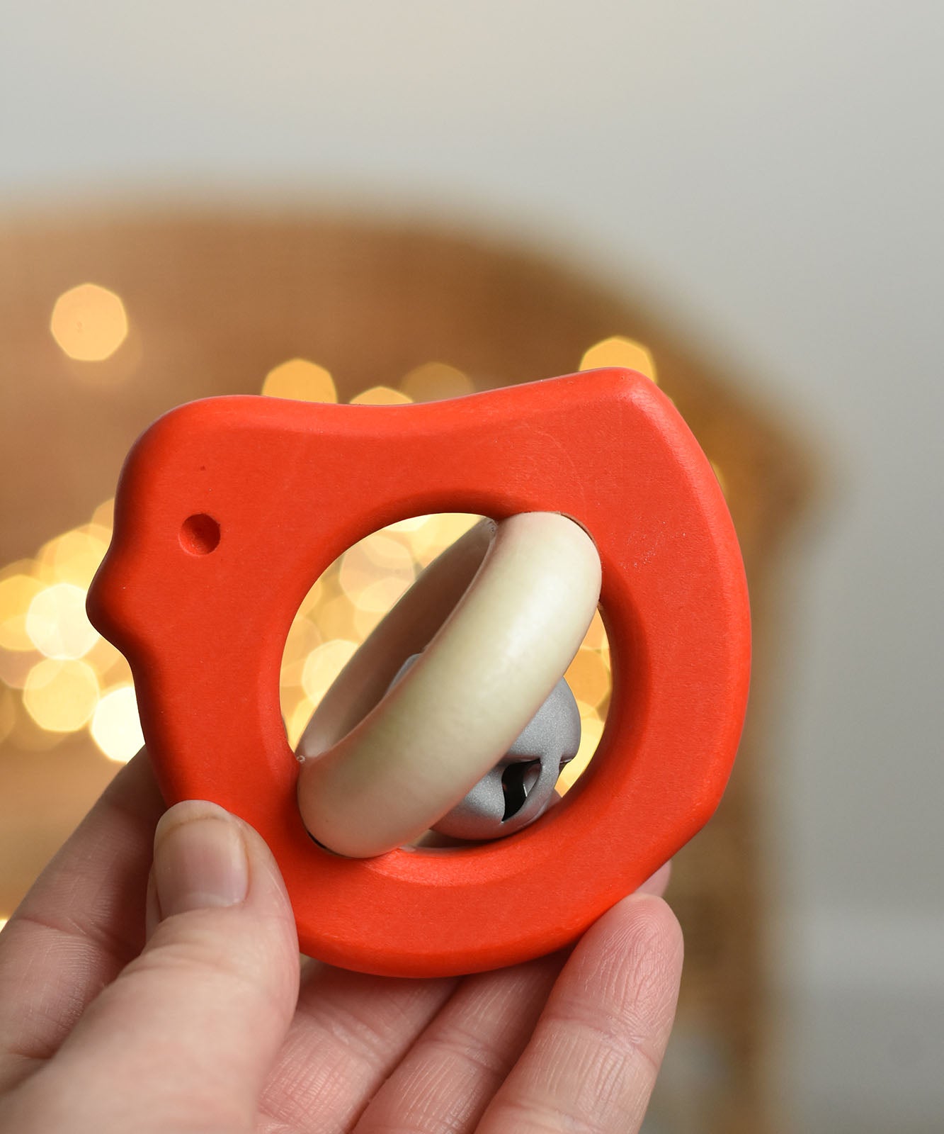 A red coloured Bajo Wooden Bird Baby Rattle with Bell shown in an adult's hand. These heirloom quality toys by Bajo are part of a wide range of wooden toys available here at Babipur. 
