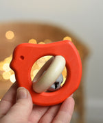 A red coloured Bajo Wooden Bird Baby Rattle with Bell shown in an adult's hand. These heirloom quality toys by Bajo are part of a wide range of wooden toys available here at Babipur. 