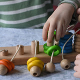 Bajo rope abacus toy with 10 pegs. Child lifting teh green wooden rings from the number 4 peg.
