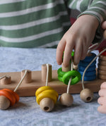 Bajo rope abacus toy with 10 pegs. Child lifting teh green wooden rings from the number 4 peg.