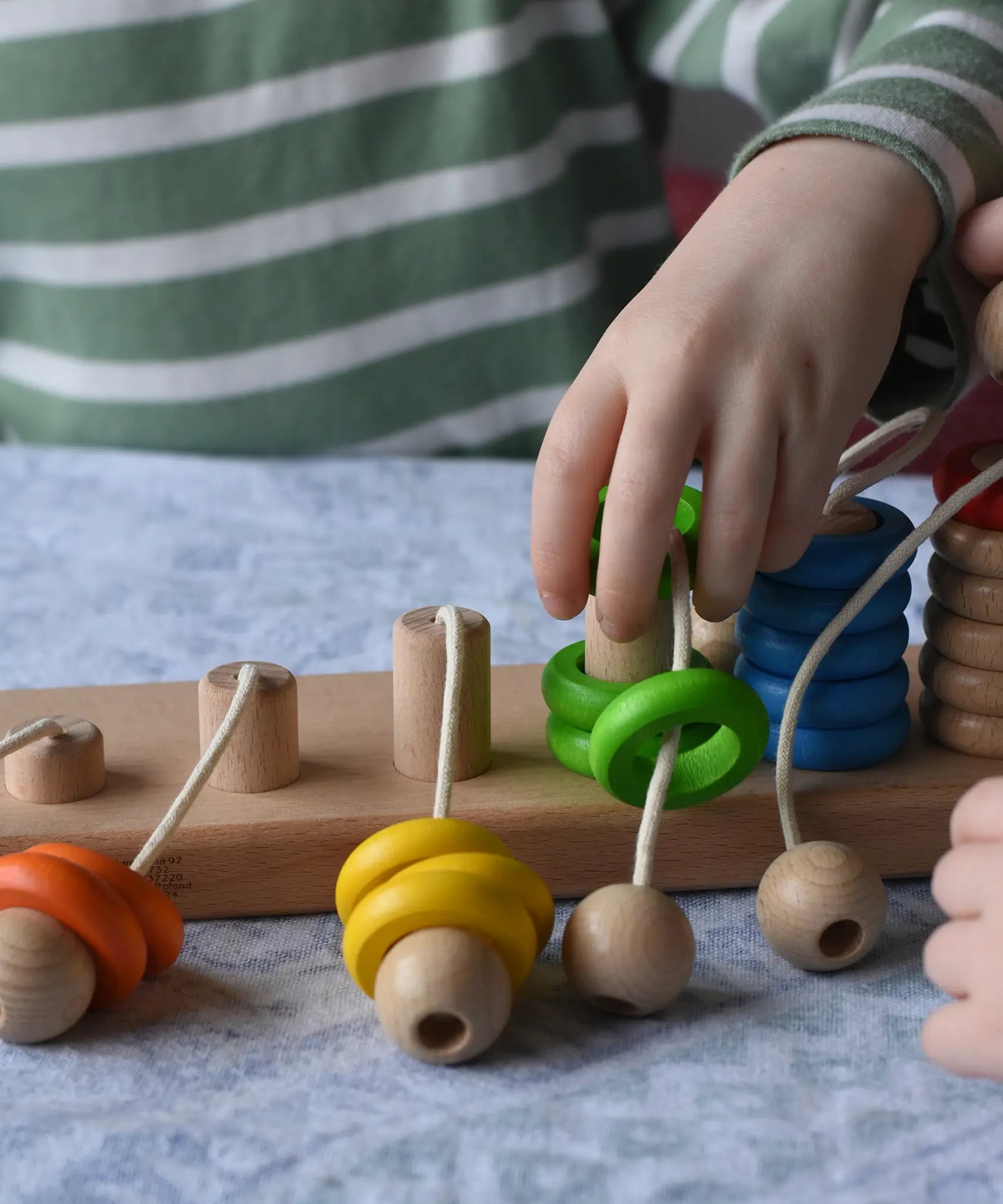 Bajo rope abacus toy with 10 pegs. Child lifting teh green wooden rings from the number 4 peg.