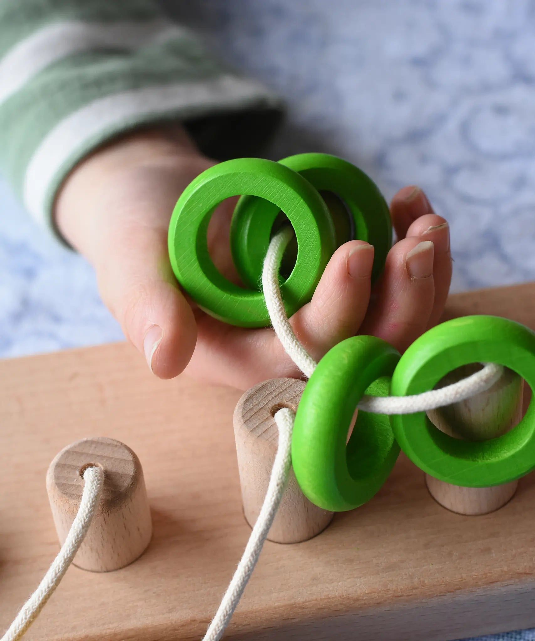 Bajo rope abacus toy with 10 pegs. Rope with green rings on in child's hand.