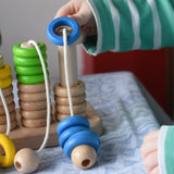 Bajo rope abacus toy with 10 pegs. Child lifting the wooden rings from the number 10 peg.