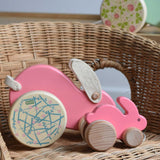 A small pink coloured Bajo rabbit placed on a wicker chair with a big pink rabbit behind it.  These heirloom quality toys by Bajo are part of a wide range of wooden toys available here at Babipur.