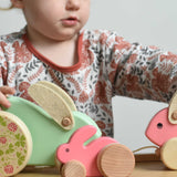 A pink coloured Bajo mini wooden rabbit on a Triclimb Miri slide. A child can be seen in th ebackground playing the two large Bajo rabbit toys.  These heirloom quality toys by Bajo are part of a wide range of wooden toys available here at Babipur.