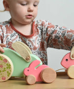 A pink coloured Bajo mini wooden rabbit on a Triclimb Miri slide. A child can be seen in th ebackground playing the two large Bajo rabbit toys.  These heirloom quality toys by Bajo are part of a wide range of wooden toys available here at Babipur.