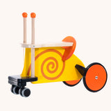 Bajo toys wooden snail ride on toy. A yellow coloured snail with orange swirl details and features and orange wheels. These heirloom quality toys by Bajo are part of a wide range of wooden toys available here at Babipur. 