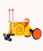 Bajo toys wooden snail ride on toy. A yellow coloured snail with orange swirl details and features and orange wheels. These heirloom quality toys by Bajo are part of a wide range of wooden toys available here at Babipur. 
