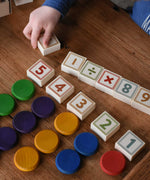 An overhead view of a child plaing with the Bajo 40 Numbers & Symbols Blocks. They have number blocks with Grapat wooden coins lined up besides them. These heirloom quality toys by Bajo are part of a wide range of wooden toys available here at Babipur. 