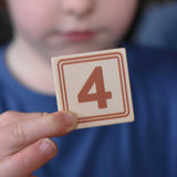A child holding up a number four block from the Bajo 40 Numbers & Symbols Blocks set in their hand. These heirloom quality toys by Bajo are part of a wide range of wooden toys available here at Babipur. 