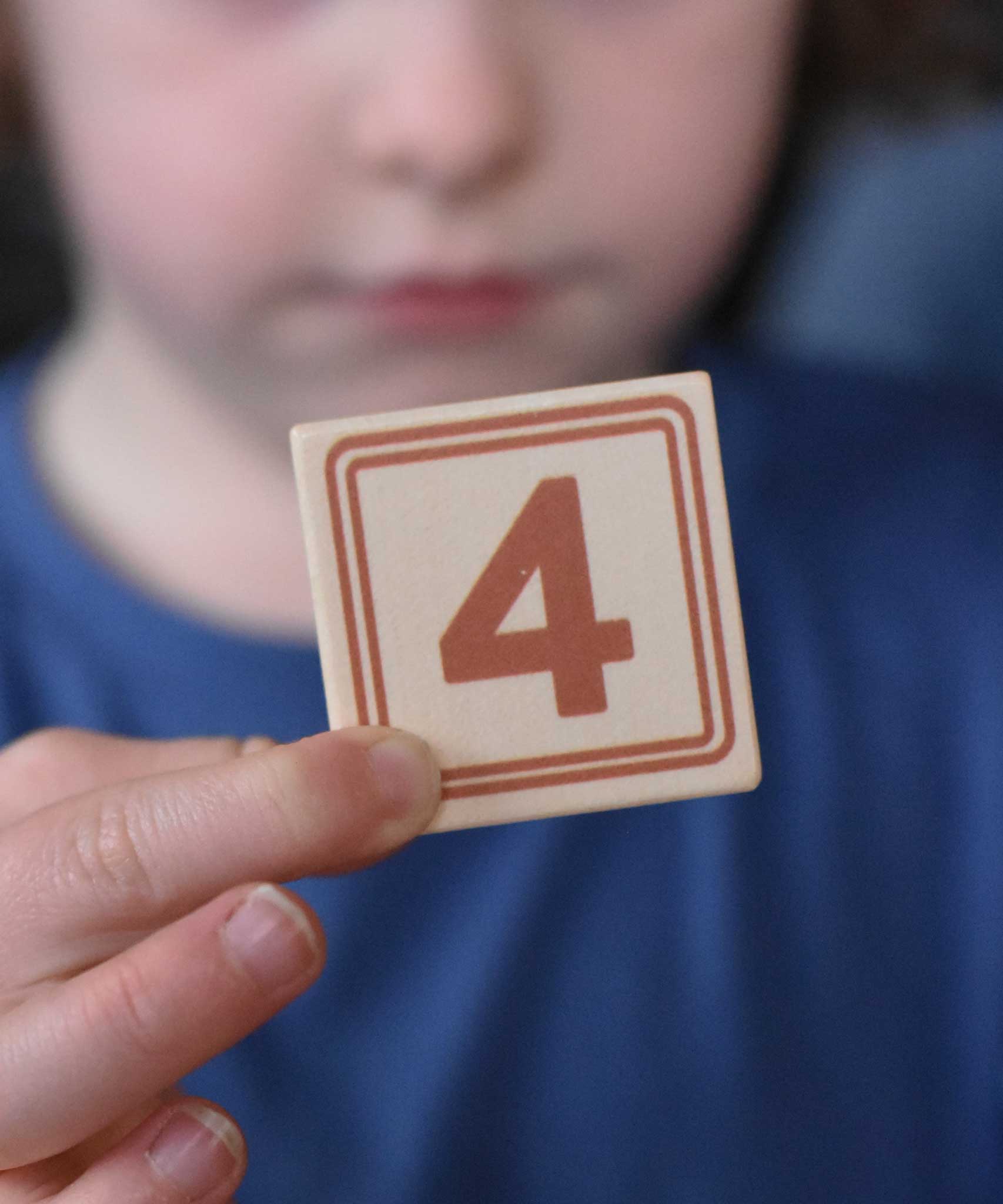 A child holding up a number four block from the Bajo 40 Numbers & Symbols Blocks set in their hand. These heirloom quality toys by Bajo are part of a wide range of wooden toys available here at Babipur. 