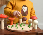 A child playing with the Bajo Wooden Mushroom Forest Peg Puzzle. The child is placing the yellow coloured mushroom on one of the green coloured pegs on the wooden base. These heirloom quality toys by Bajo are part of a wide range of wooden toys available here at Babipur. 