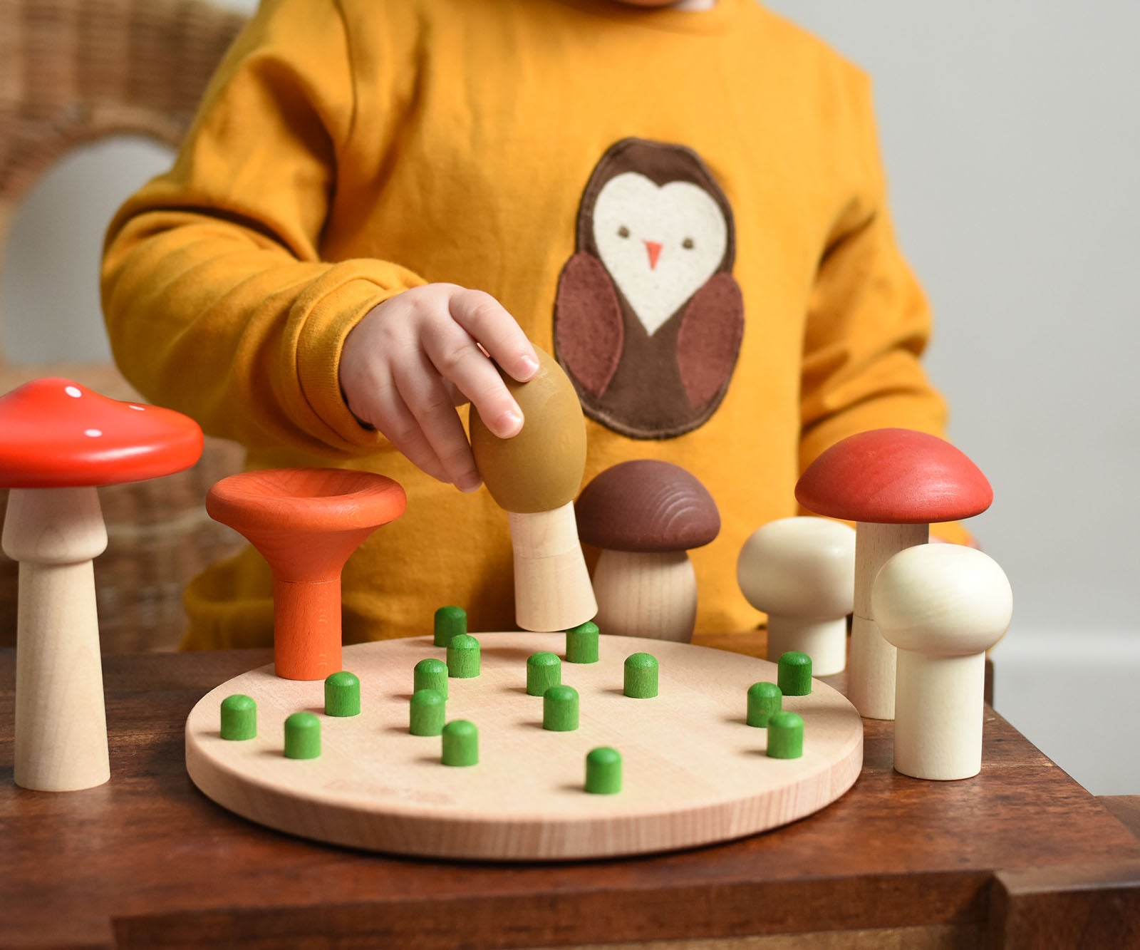 A child playing with the Bajo Wooden Mushroom Forest Peg Puzzle. The child is placing the yellow coloured mushroom on one of the green coloured pegs on the wooden base. These heirloom quality toys by Bajo are part of a wide range of wooden toys available here at Babipur. 