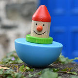 Bajo roly poly wobbling dwarf wooden baby toy placed on a stone wall outdoors.