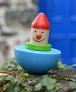 Bajo roly poly wobbling dwarf wooden baby toy placed on a stone wall outdoors.