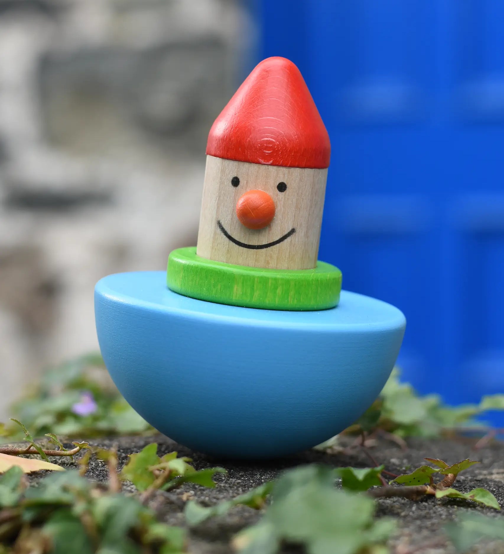 Bajo roly poly wobbling dwarf wooden baby toy placed on a stone wall outdoors.