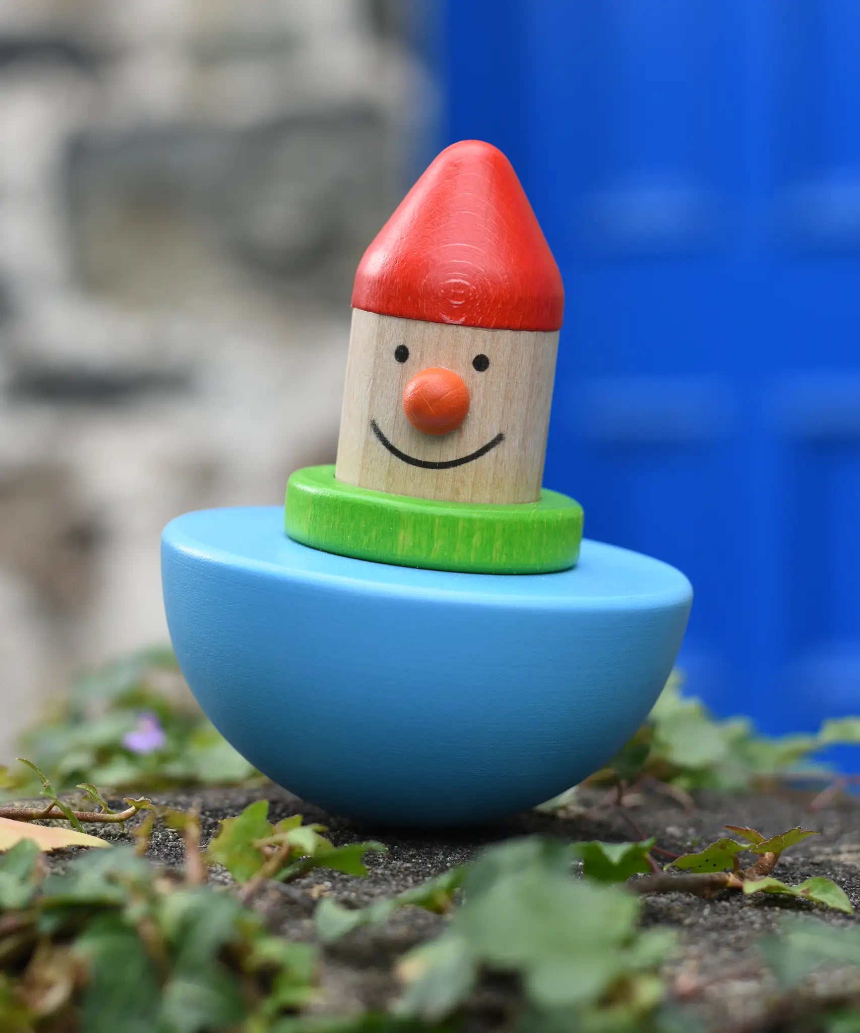 Bajo roly poly wobbling dwarf wooden baby toy placed on a stone wall outdoors.