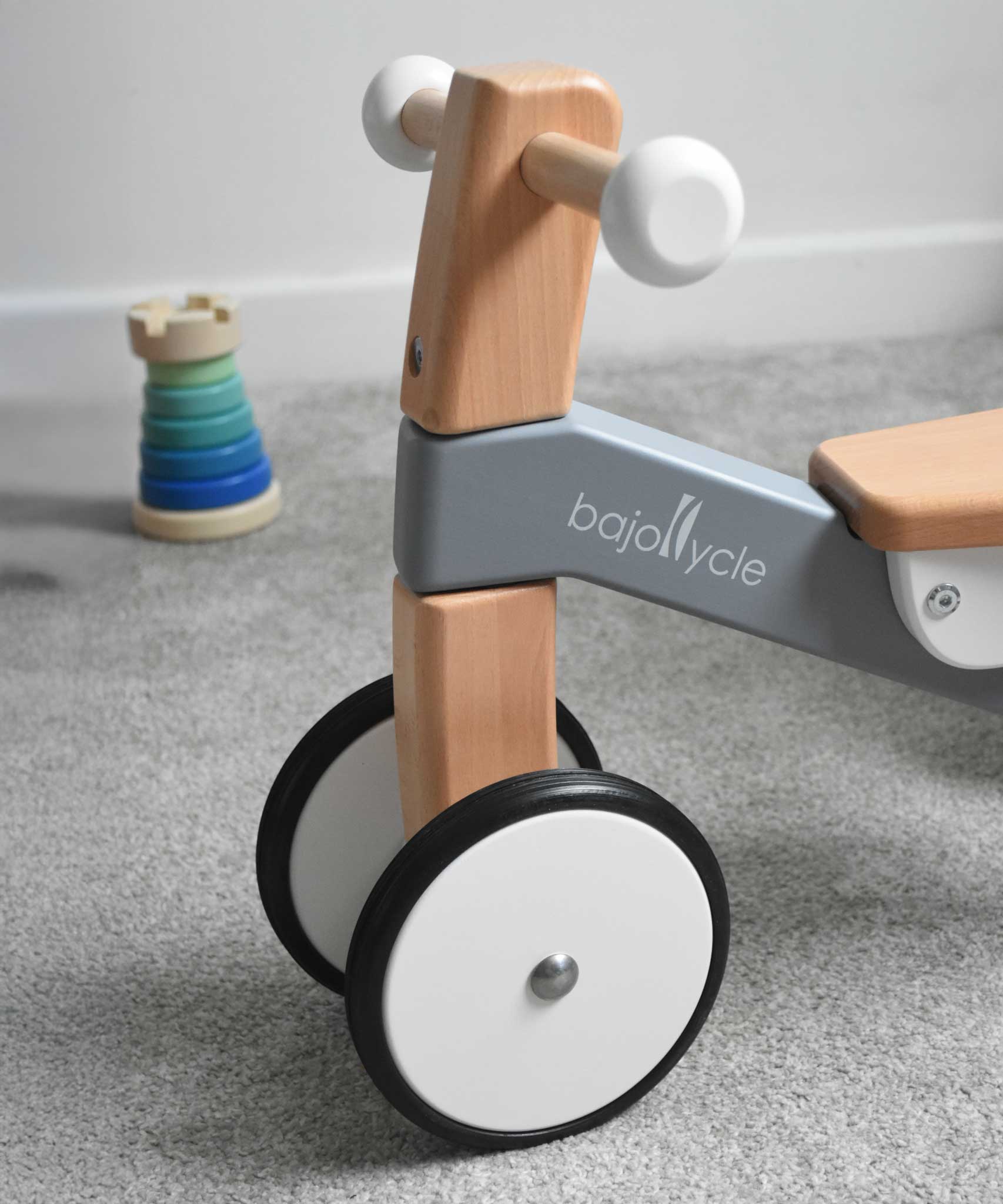 A close up of the front of the Bajo Toys wooden Cycle toddler Ride-On in the monochrome, white and grey colourway. The wheels are white with a black rubber outer.

The wooden ride on cycle is part of a wode range of wooden toys available here at Babipur. 