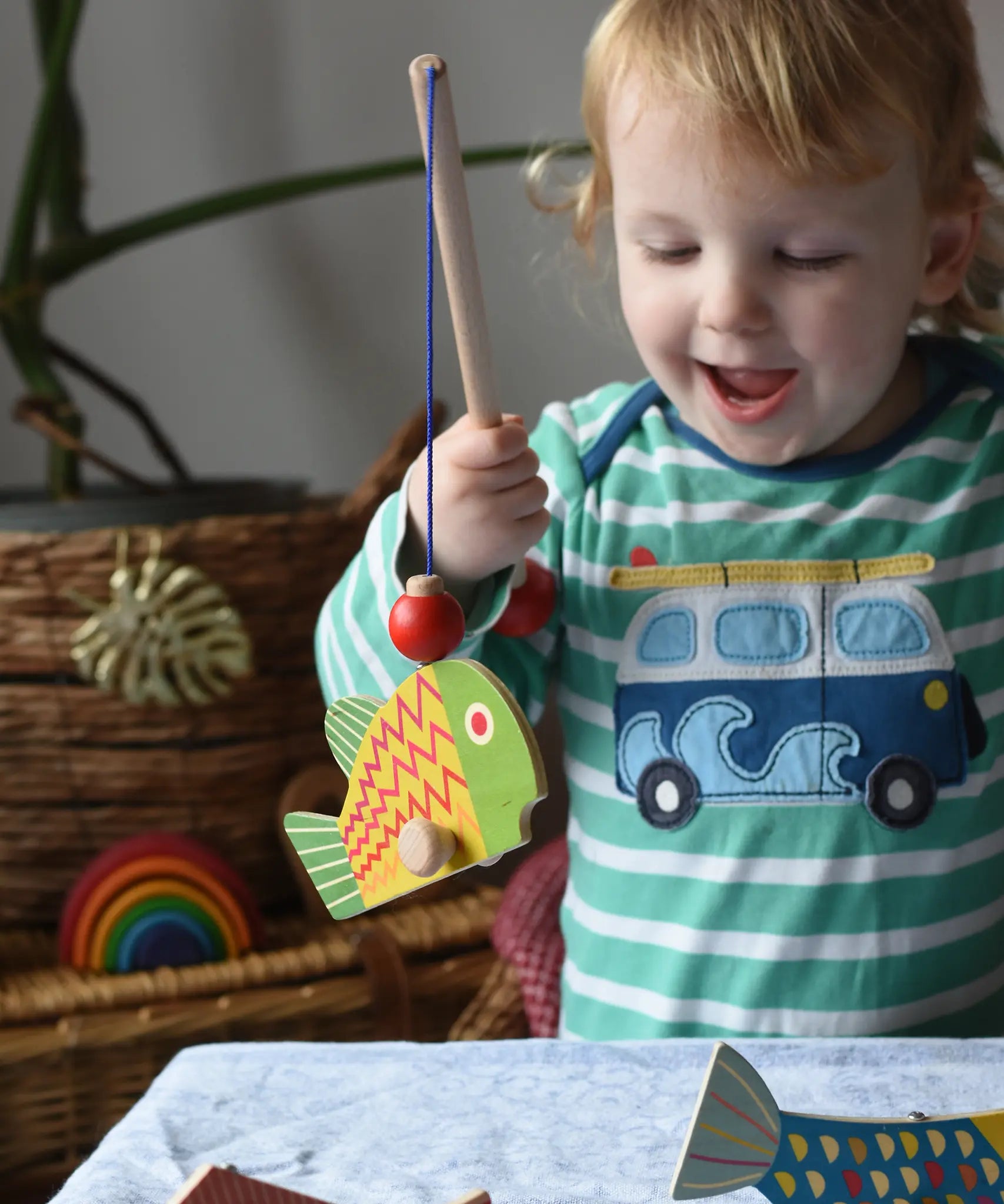 Bajo magnetic fishing game toy. Child holding wooden rod with yellow and green fish attached.