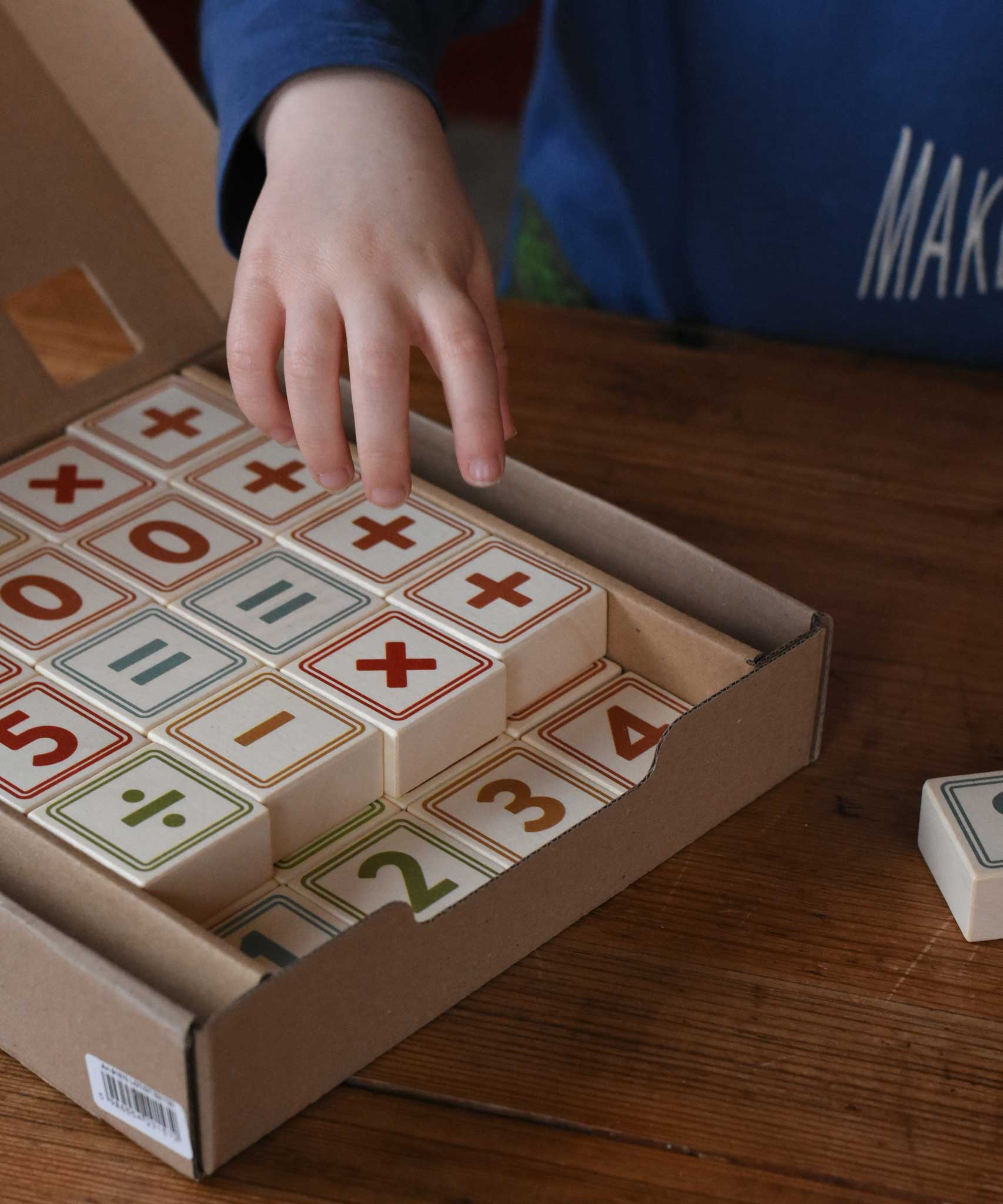 A child reaching for the blocks from the box of Bajo 40 Numbers & Symbols Blocks set. These heirloom quality toys by Bajo are part of a wide range of wooden toys available here at Babipur. 