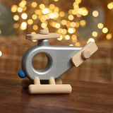A silver coloured Bajo Police Helicopter wooden toy placed on a small wooden table. These heirloom quality toys by Bajo are part of a wide range of wooden toys available here at Babipur. 