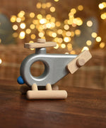 A silver coloured Bajo Police Helicopter wooden toy placed on a small wooden table. These heirloom quality toys by Bajo are part of a wide range of wooden toys available here at Babipur. 