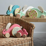 A collection of Bajo wooden rabbit toys small and big. Some have been placed on a wicker child's chair with some placed on a Triclimb Miri slide behind them.  These heirloom quality toys by Bajo are part of a wide range of wooden toys available here at Babipur.