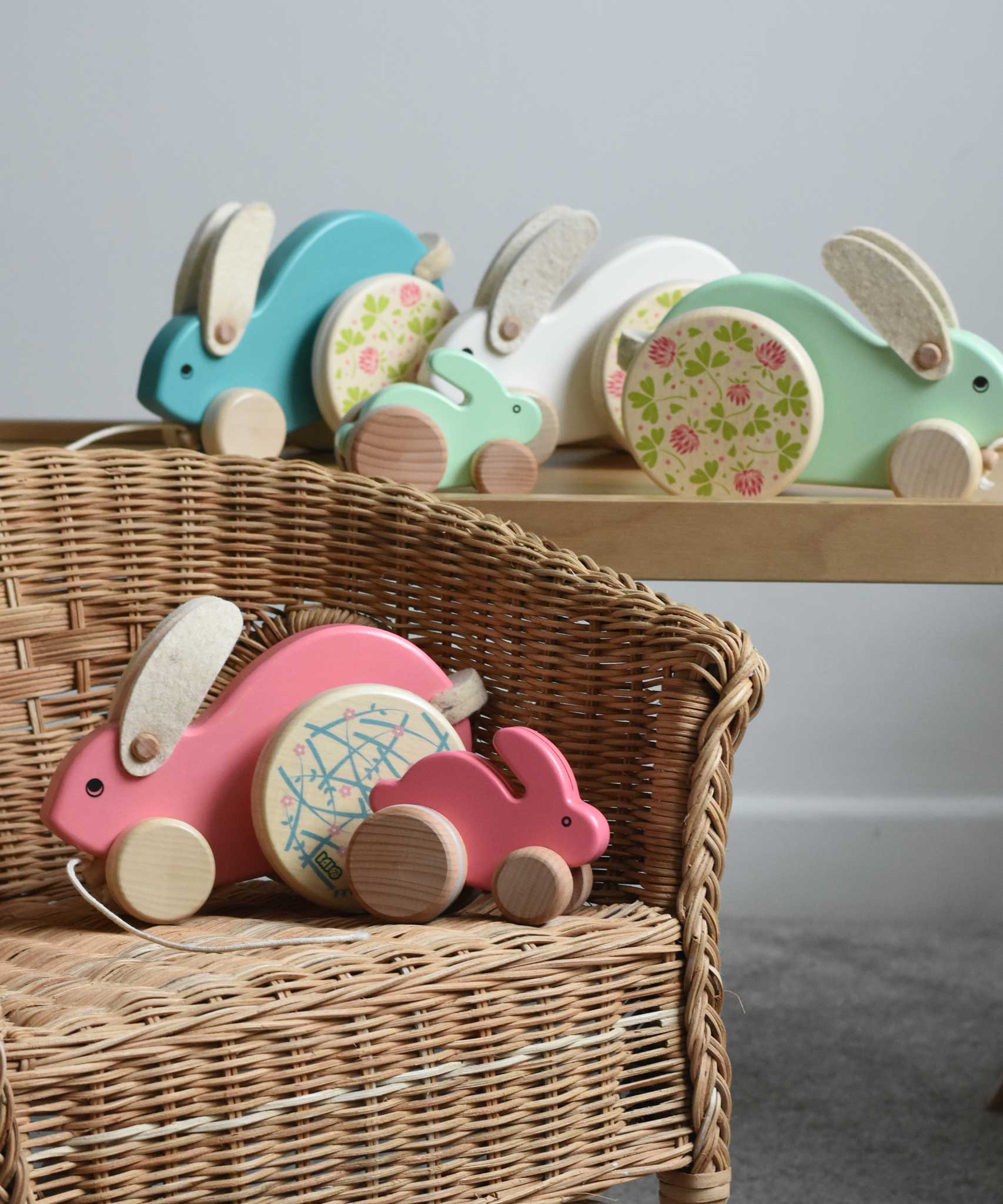 A collection of Bajo wooden rabbit toys small and big. Some have been placed on a wicker child's chair with some placed on a Triclimb Miri slide behind them.  These heirloom quality toys by Bajo are part of a wide range of wooden toys available here at Babipur.